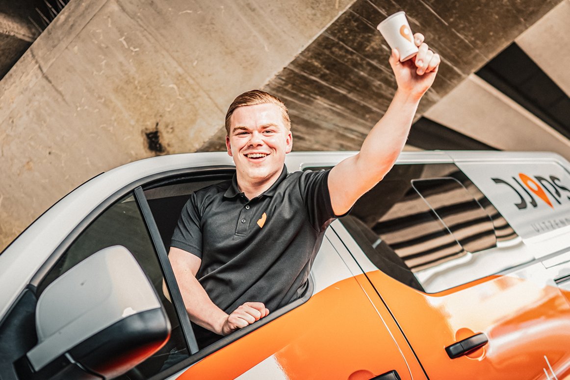 Medewerker van Djops lacht vanuit een auto en laat zien dat werkplezier centraal staat bij uitzenden via Djops.